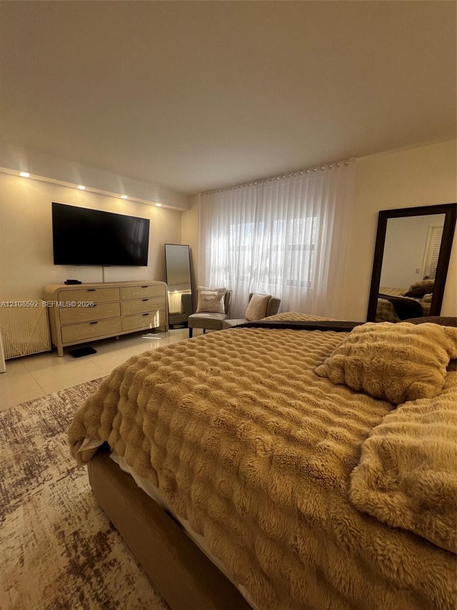 Recessed lighting, light-toned tile flooring, and a window treatment spanning the width of the wall