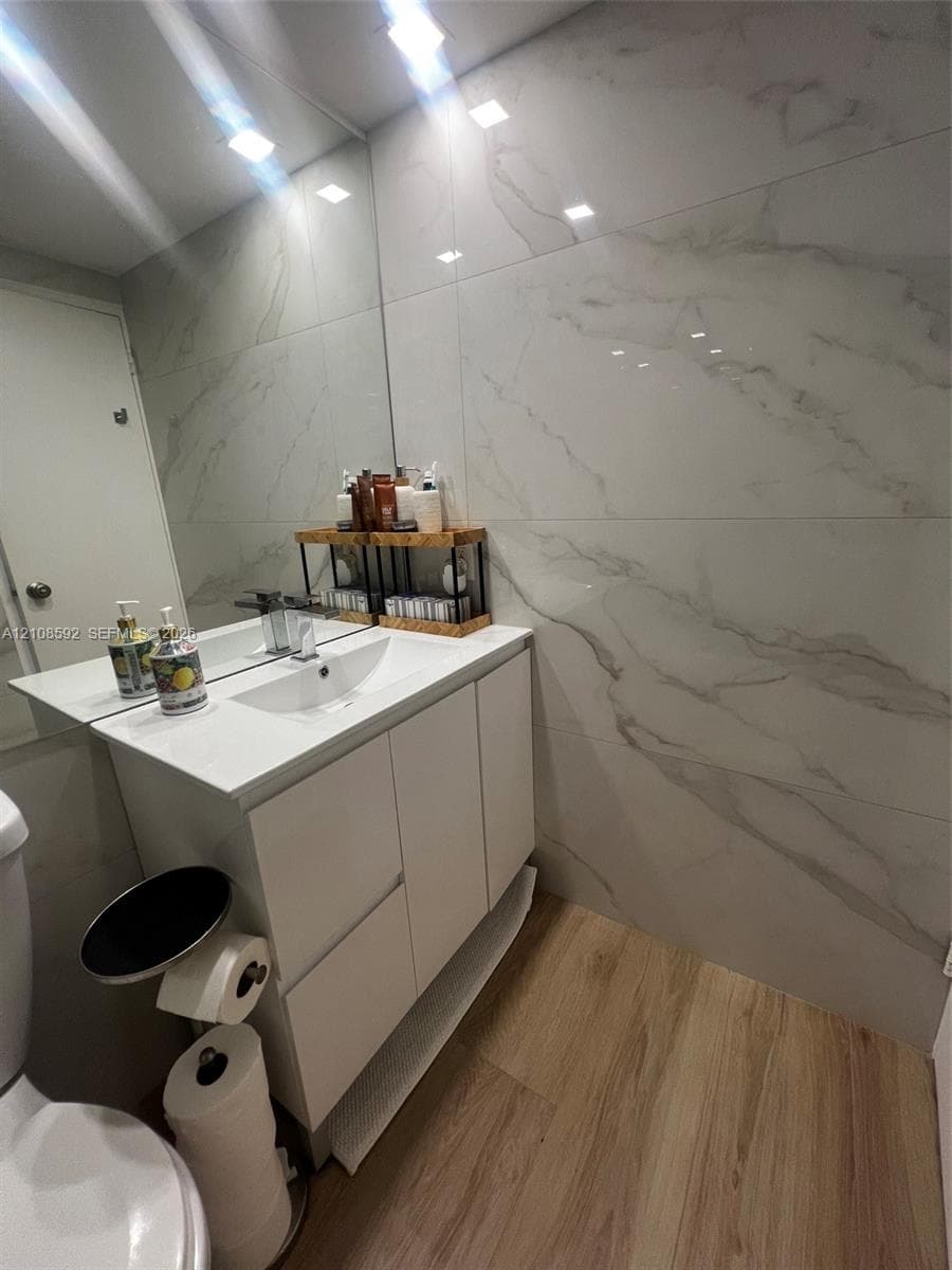 White vanity with integrated rectangular sink and polished chrome faucet, large-format veined wall tile, wood-finish flooring, and wall-to-wall mirror