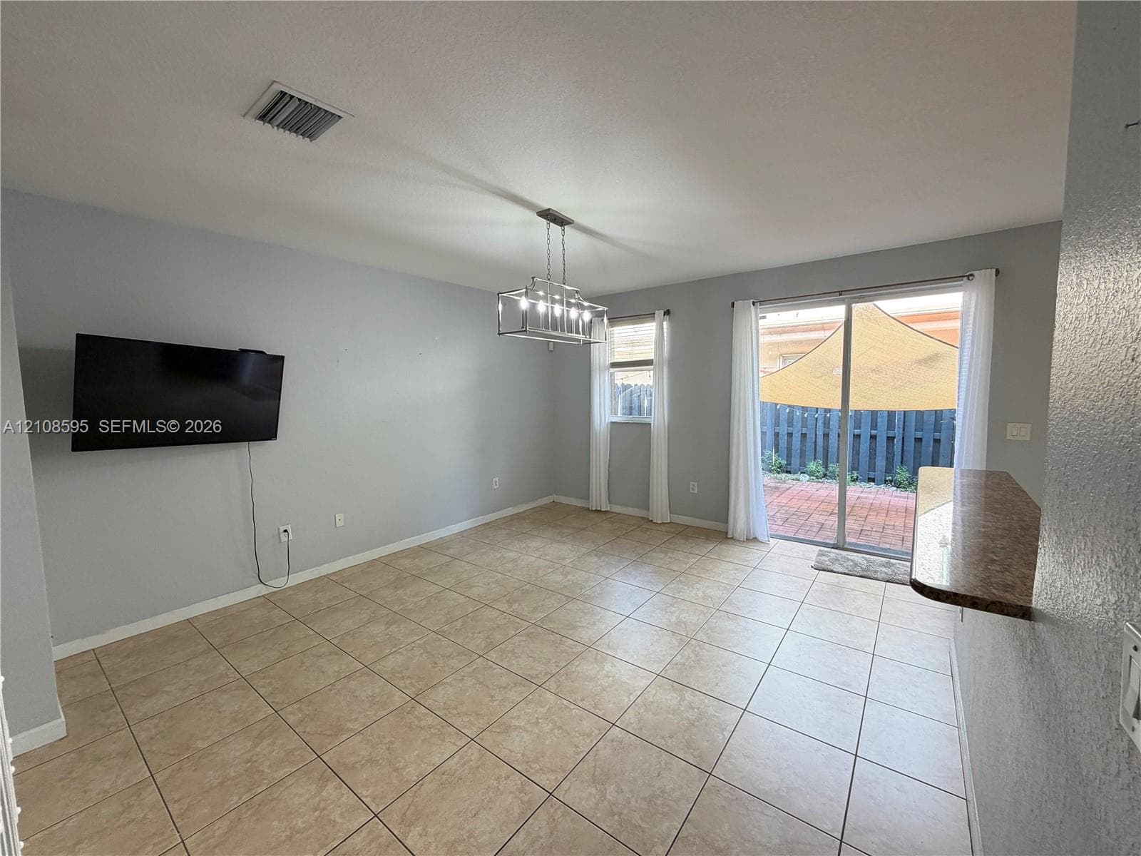 Ceramic tile flooring, industrial-style multi-light chandelier, sliding glass door, and a built-in stone-finish counter