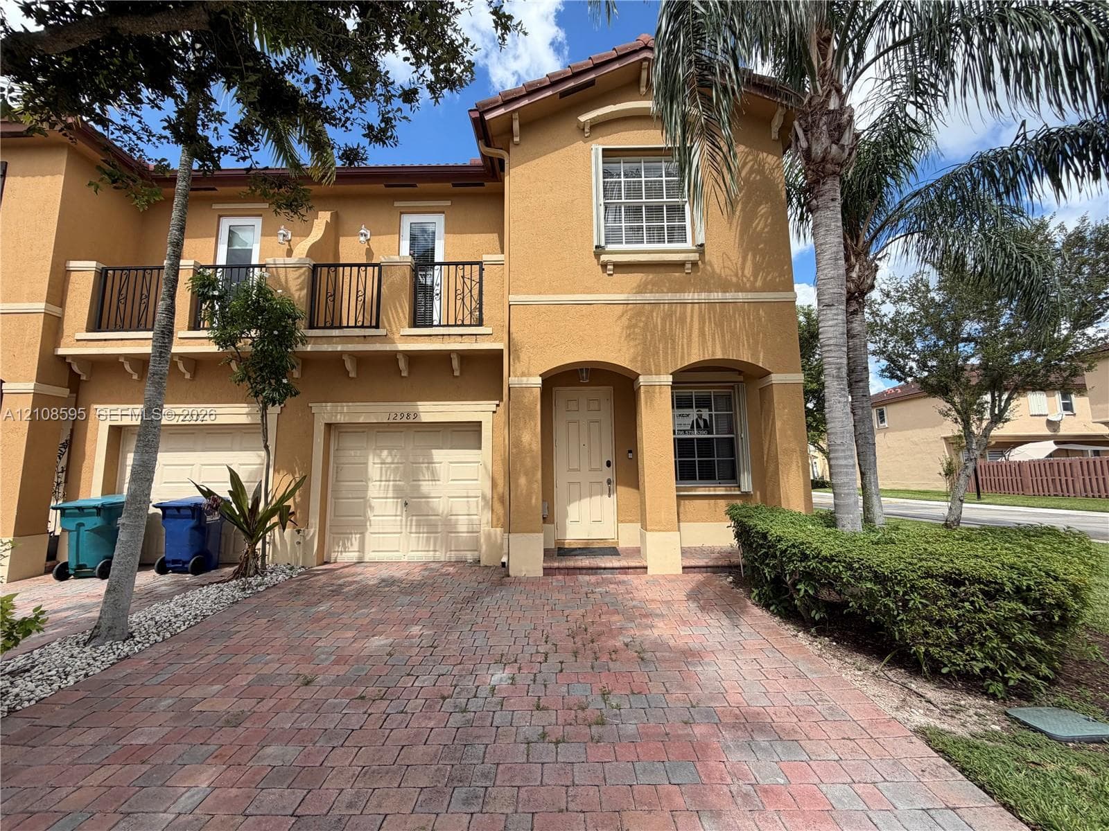 Stucco exterior featuring a paved driveway, tile roof, second-story balcony with metal railings, and arched entryway