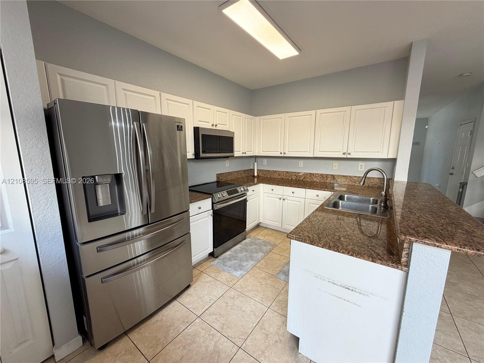 Kitchen featuring white cabinetry, stone-finish countertops, tile flooring, stainless steel French-door refrigerator, and an integrated stainless steel sink with a high-arch faucet