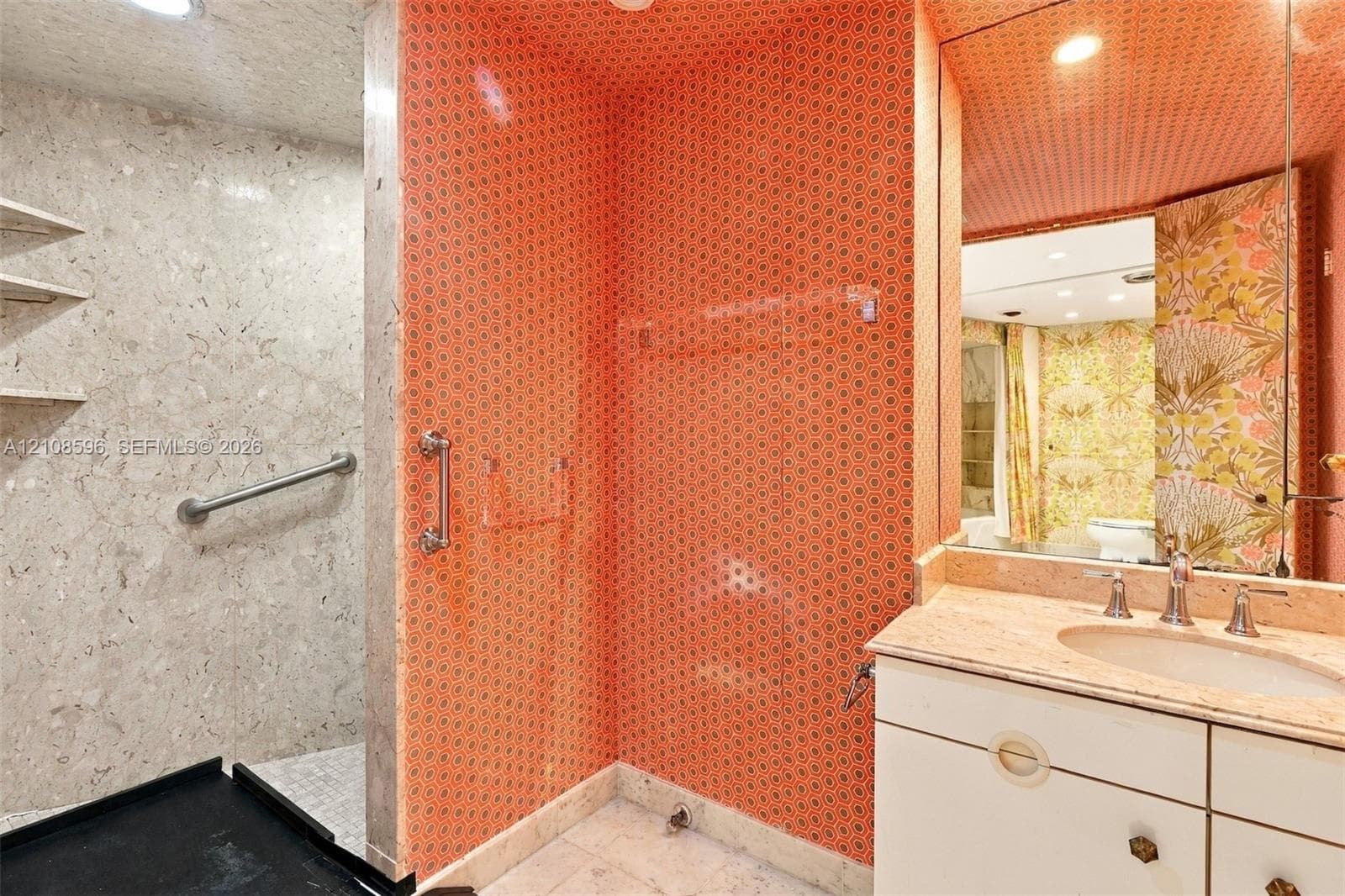 Bathroom featuring a stone-finish walk-in shower with integrated grab bar, vanity with stone countertop and undermount sink, recessed lighting, and expansive wall-to-wall mirror