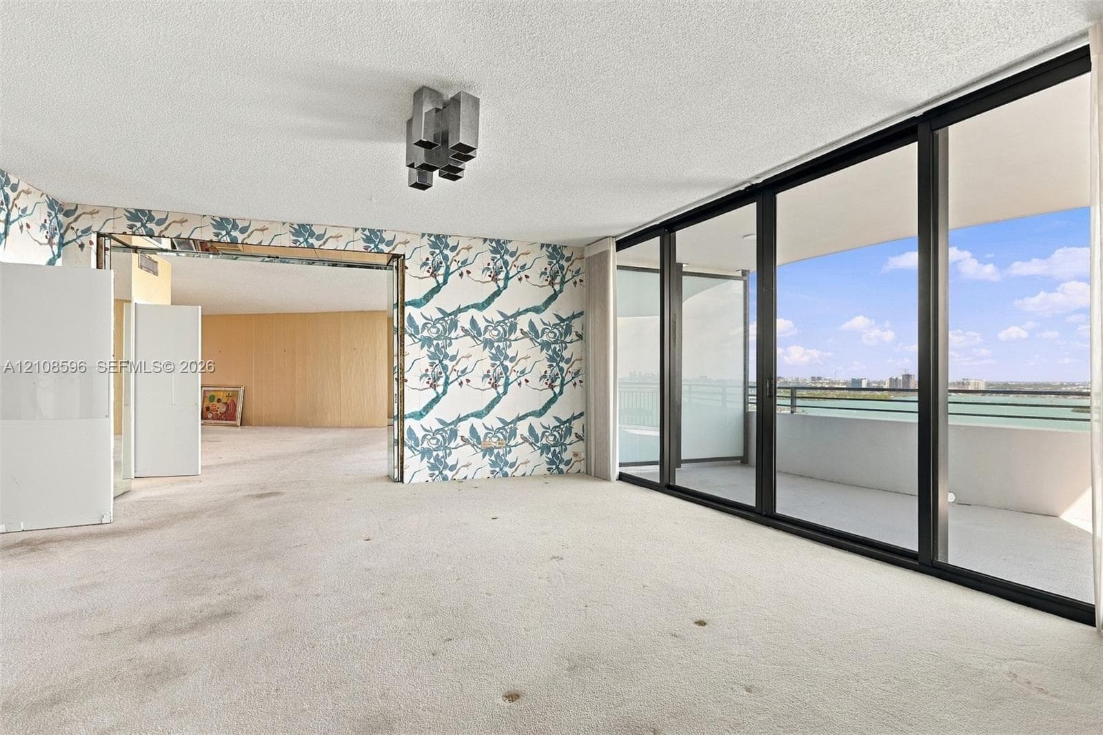 Floor-to-ceiling glass sliding doors opening to an expansive private balcony, featuring a multi-panel black frame and geometric ceiling-mounted lighting
