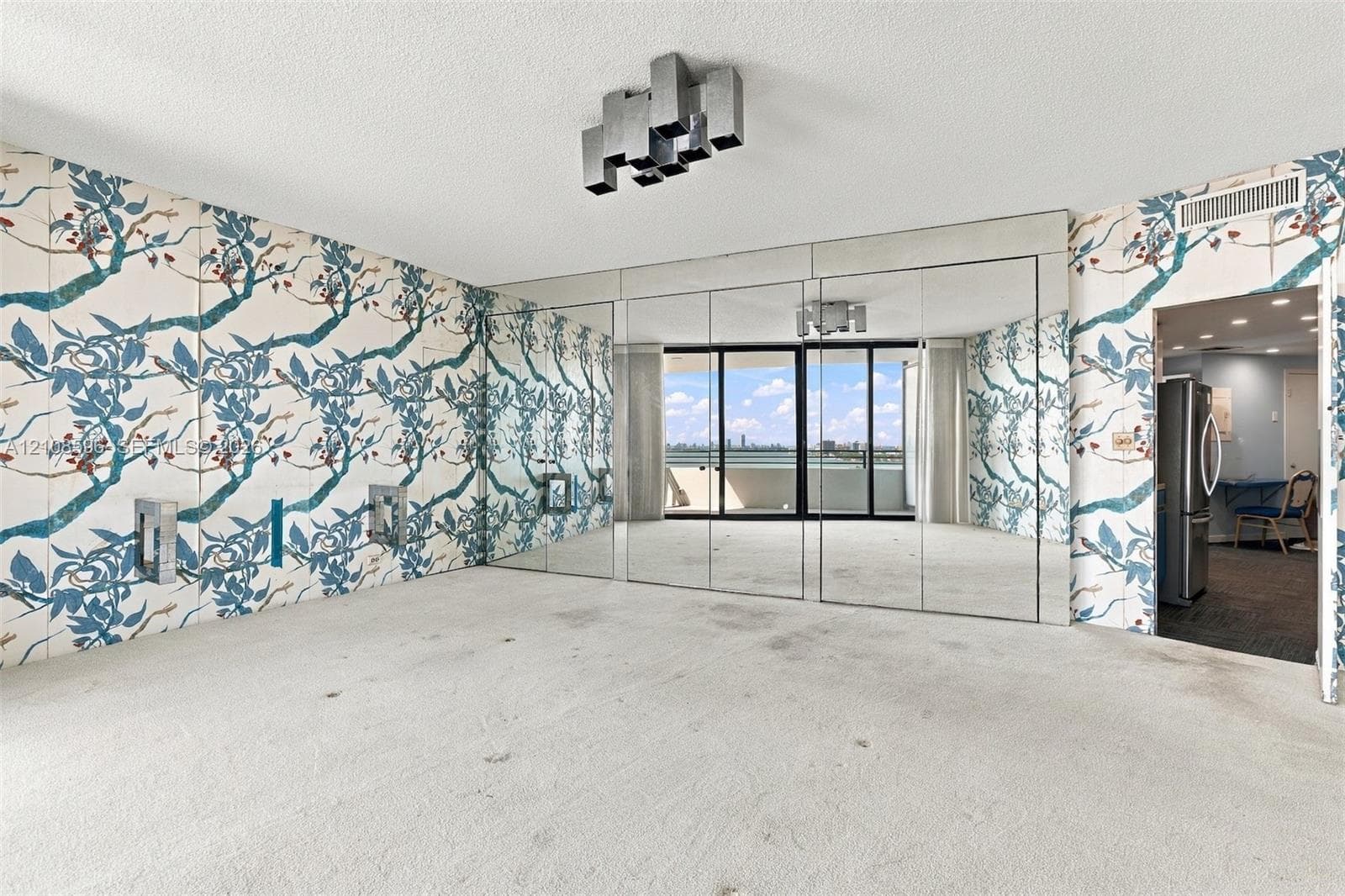 Living area featuring floor-to-ceiling mirrored wall panels, patterned wallpaper, a structural sliding glass door, and a geometric ceiling-mounted light fixture