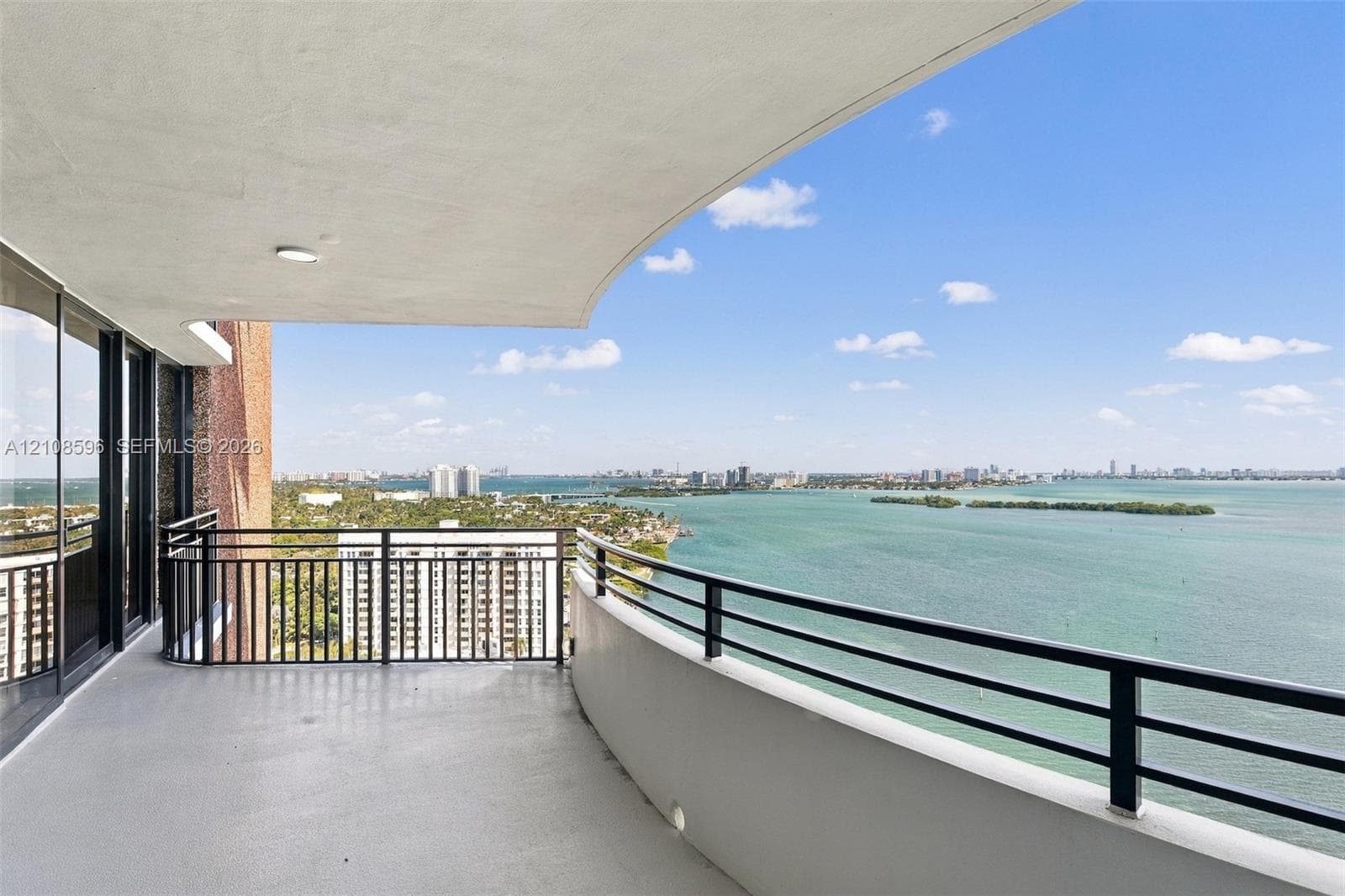 Curved open-air balcony featuring a concrete floor, black metal railing, and recessed ceiling lighting