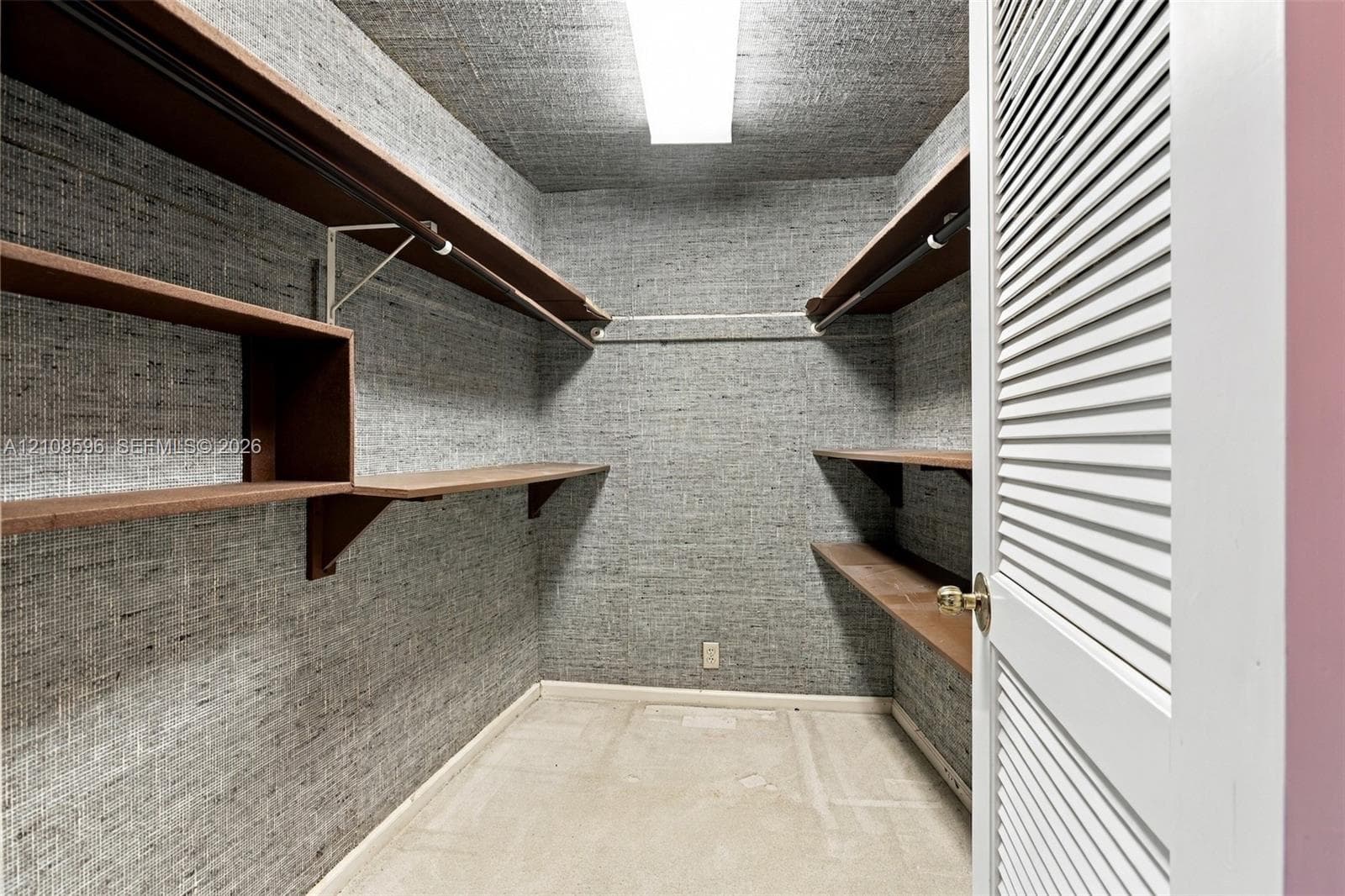 Walk-in closet featuring textured wall covering, multi-level wood-finish shelving, integrated hanging rods, and a white louvered door