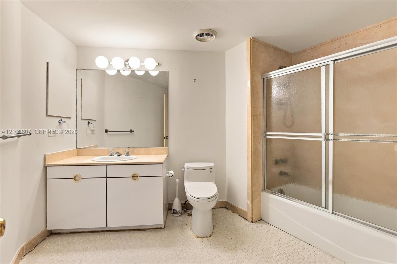 Bathroom featuring a vanity with integrated sink and stone-surfaced countertop, wall-to-wall mirror, five-light fixture, and a tub-shower combination with sliding glass doors and stone surround
