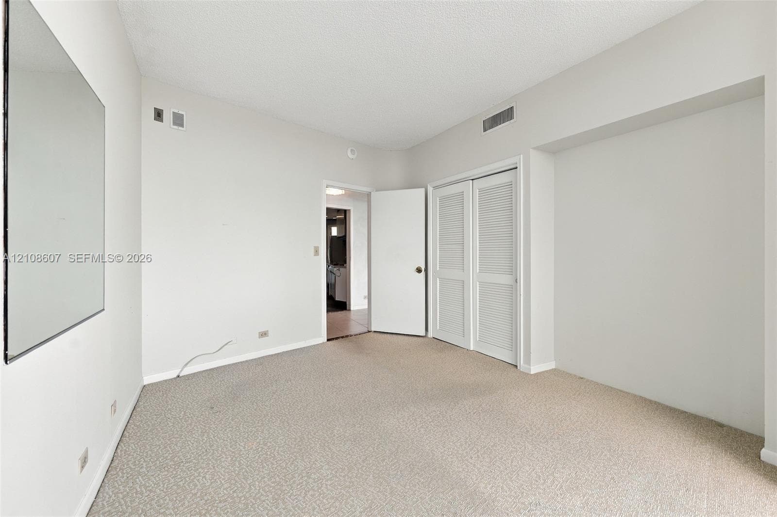 Room featuring neutral wall-to-wall carpeting, a large wall-mounted mirror, and a double-door closet with louvered panels