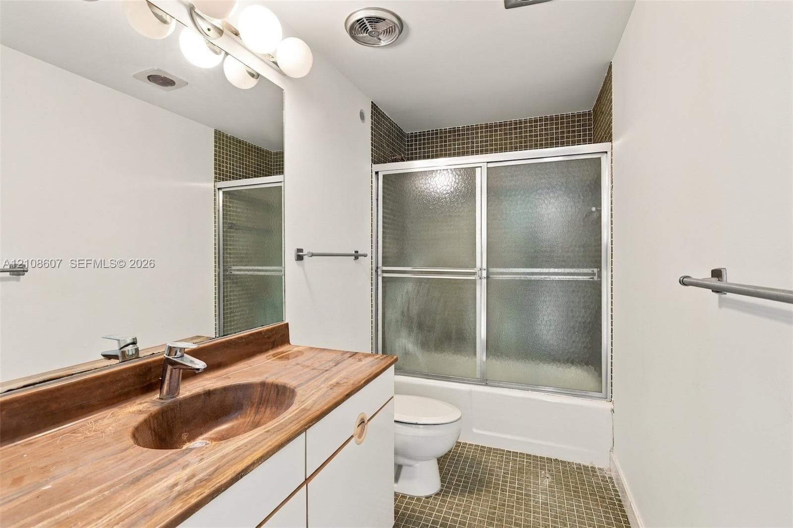 Bathroom featuring a wood-finish vanity countertop with an integrated oval sink, a wall-to-wall vanity mirror, a tub-shower combination with sliding glass doors, and tiled flooring