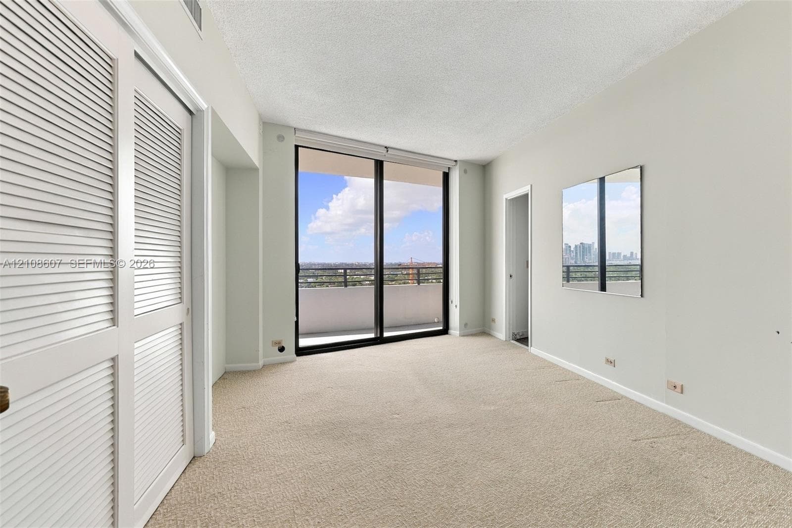 Interior space featuring floor-to-ceiling sliding glass doors, private balcony, dual-paneled louvered closet doors, and wall-mounted mirror