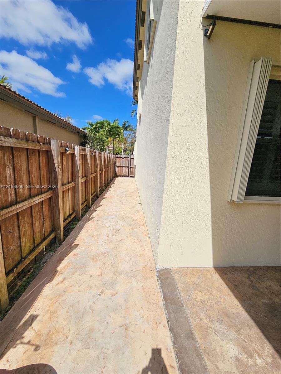 Stamped concrete side walkway featuring a wood privacy fence and exterior wall-mounted lighting