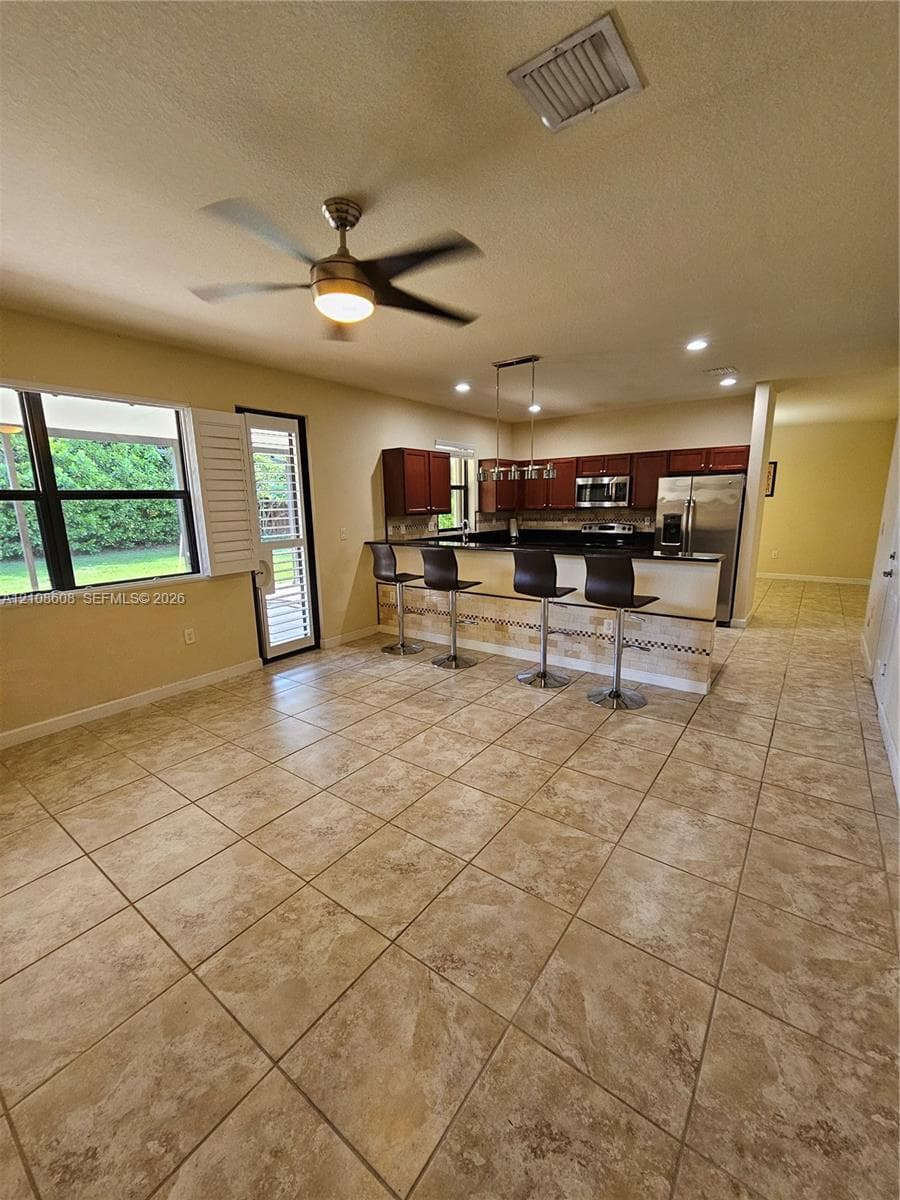 Kitchen featuring dark wood cabinetry, a stone-accented breakfast bar, stainless steel appliances, large-format tile flooring, and a ceiling fan