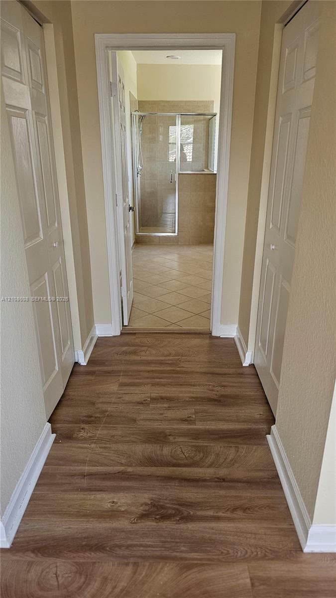 Wood-finish flooring, two sets of paneled closet doors, and tiled flooring leading to a glass-enclosed shower