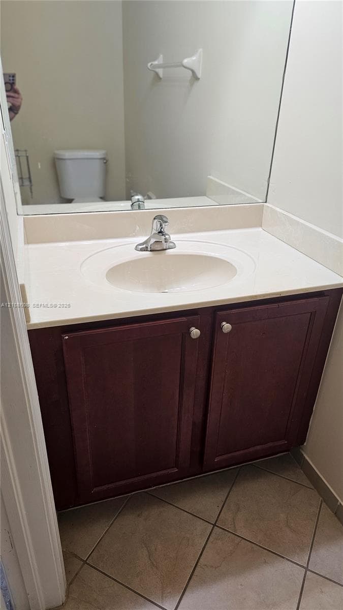 Bathroom vanity featuring a dark wood-finish cabinet, integrated basin, countertop with matching backsplash, and tile flooring
