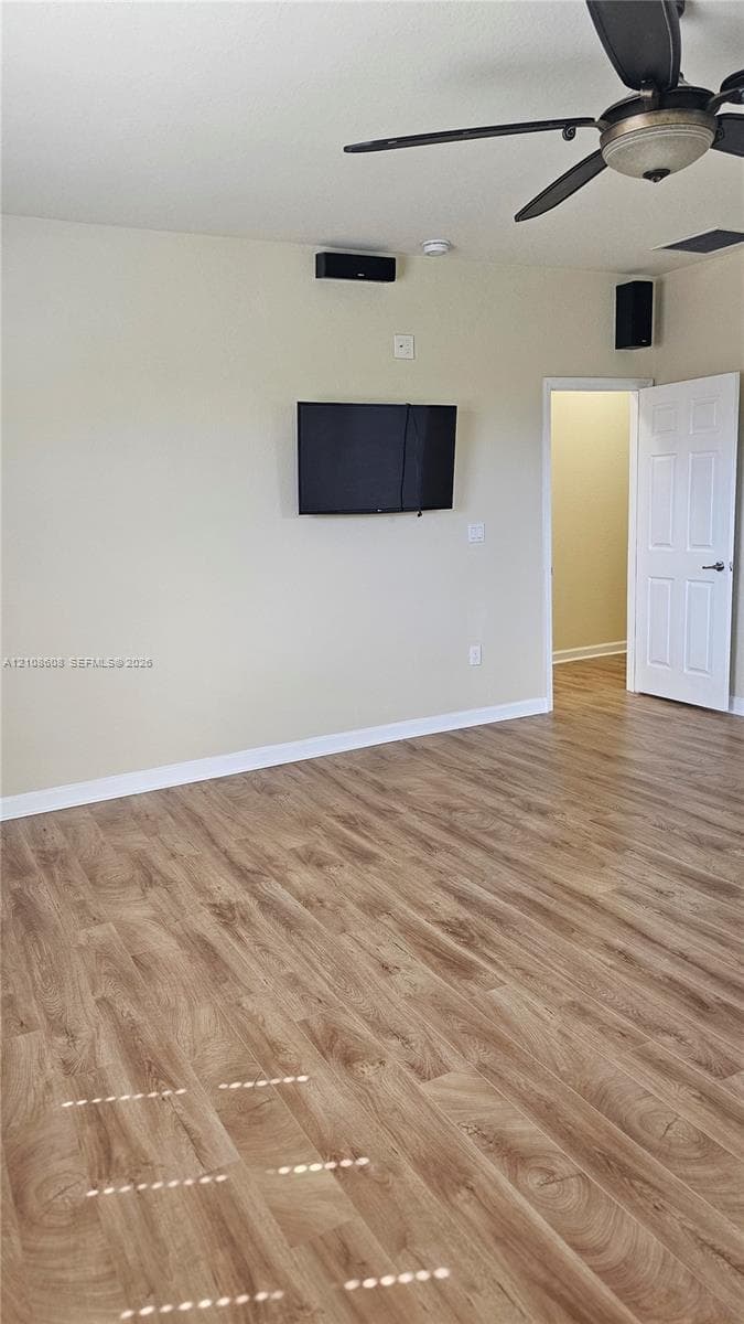 Wood-finish flooring, ceiling fan with integrated lighting, wall-mounted display hardware, and a paneled interior door