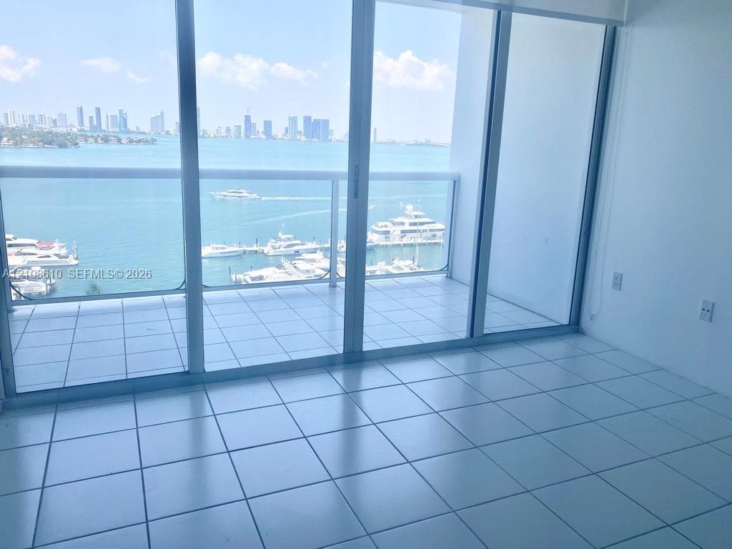 Floor-to-ceiling sliding glass doors, white ceramic tile flooring, and a private balcony featuring a glass railing