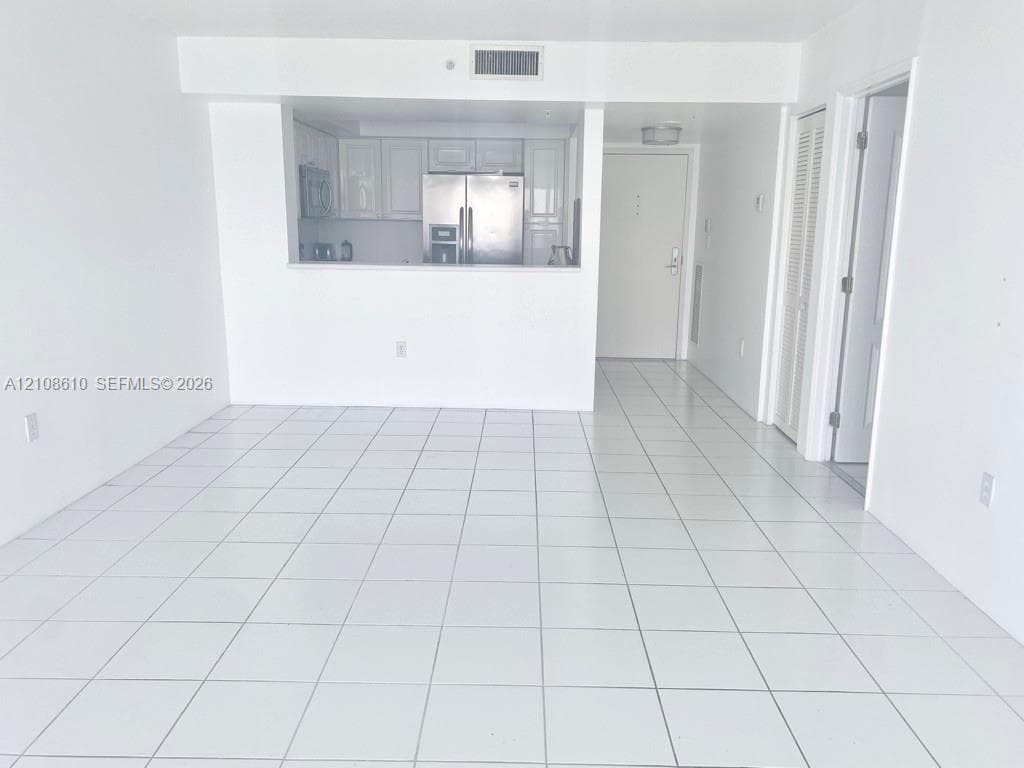 Open-concept interior featuring white ceramic floor tiling, white cabinetry, stainless steel kitchen appliances, and bi-fold closet doors