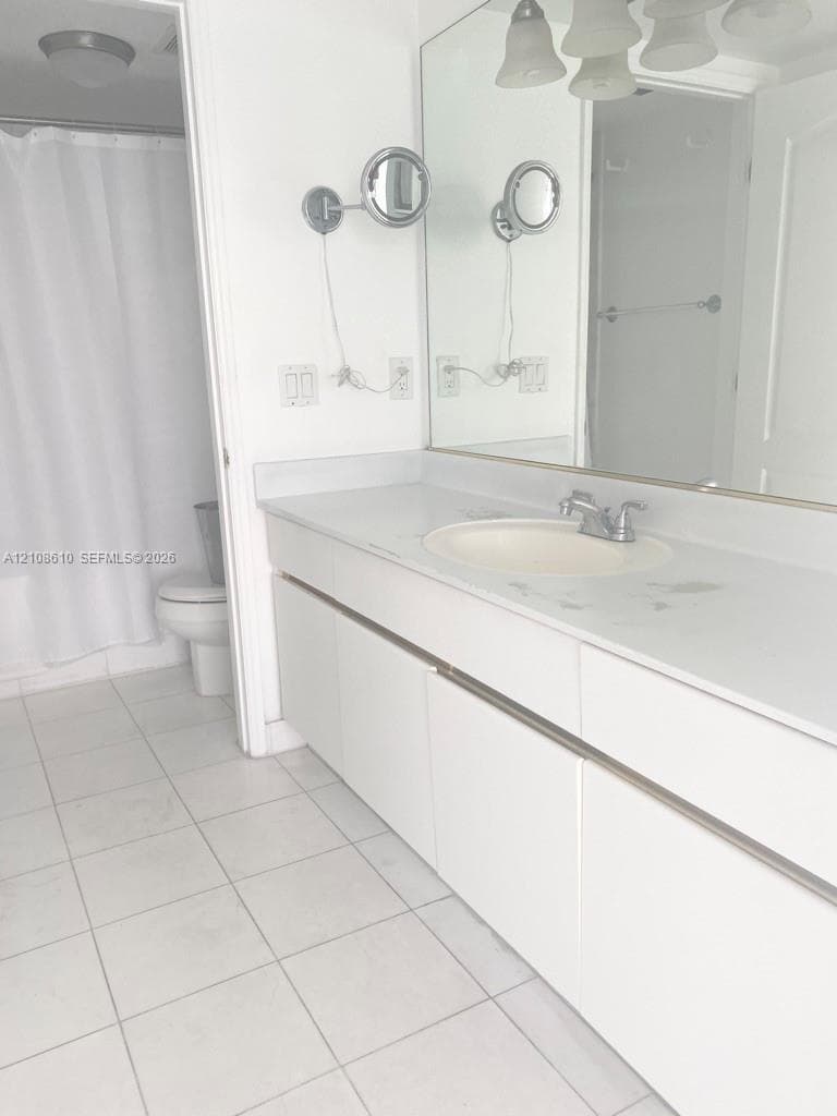 Bathroom featuring a white vanity with a solid surface countertop, an integrated sink, dual wall-mounted magnifying mirrors, a large wall-to-wall mirror, and ceramic tile flooring