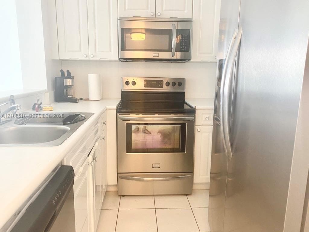 Kitchen featuring white cabinetry, stainless steel appliances, a glass-top electric range, a built-in microwave, and tile flooring