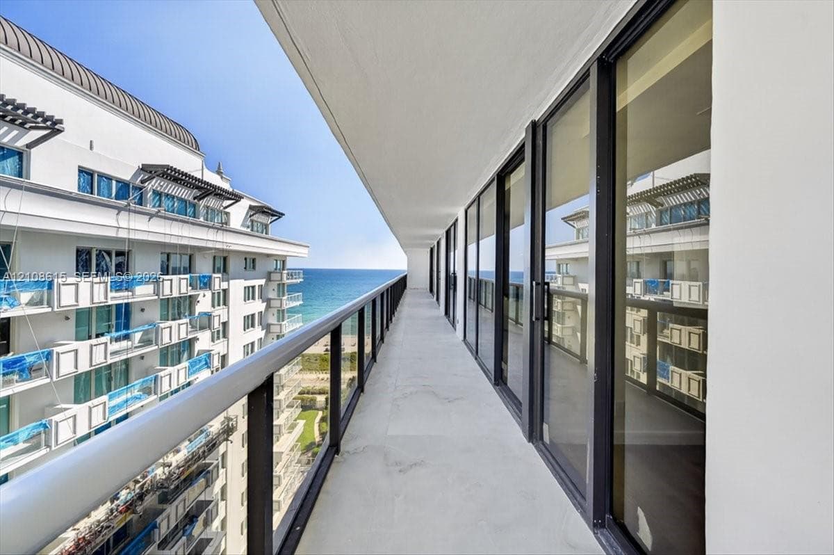 Expansive covered balcony featuring glass panel railings, concrete flooring, and full-height sliding glass doors