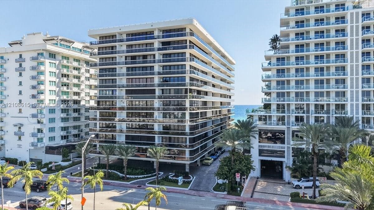 Multi-story residential building featuring floor-to-ceiling glass windows, wraparound balconies with railings, and palm-lined grounds