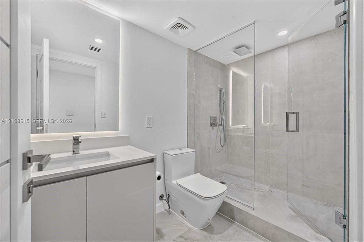 Modern bathroom featuring a floating vanity with a light-toned countertop, a seamless walk-in shower with a glass enclosure, large-format tile flooring, and backlit wall mirror
