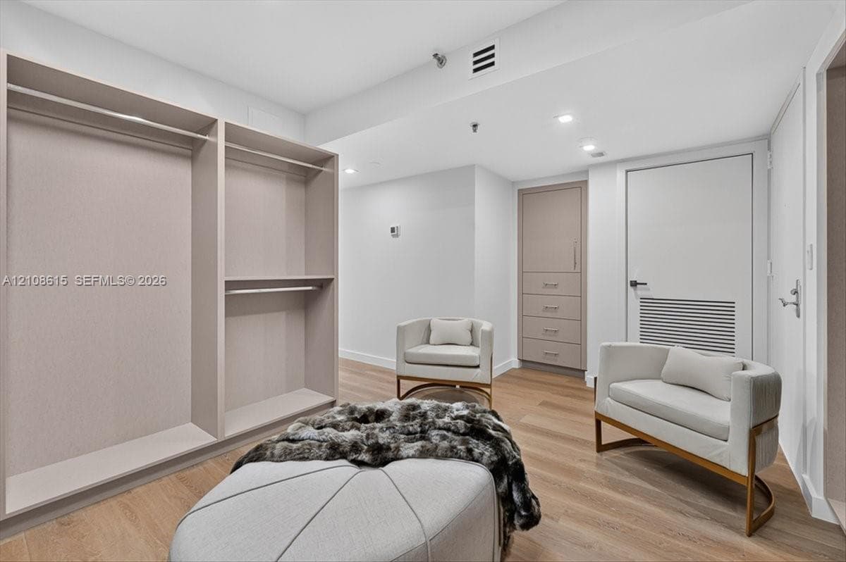 Custom dressing area featuring built-in cabinetry, floor-to-ceiling closet organization, recessed ceiling lighting, and wood-finish flooring