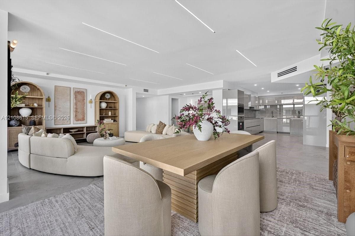 Open-concept interior featuring linear recessed ceiling lighting, built-in arched shelving units, neutral large-format tile flooring, and integrated kitchen cabinetry