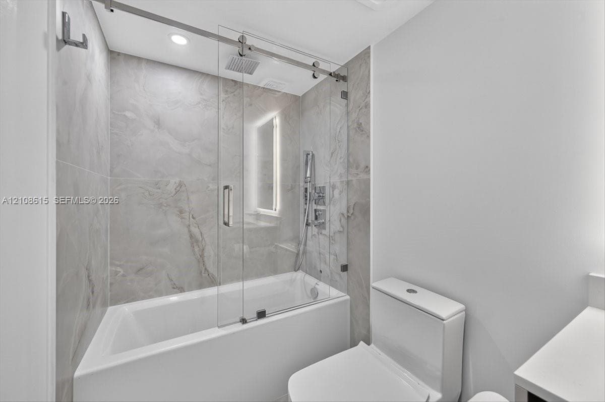 Shower with glass sliding enclosure, floor-to-ceiling stone-finish tile surround, ceiling-mounted rainfall showerhead, and integrated handheld fixture