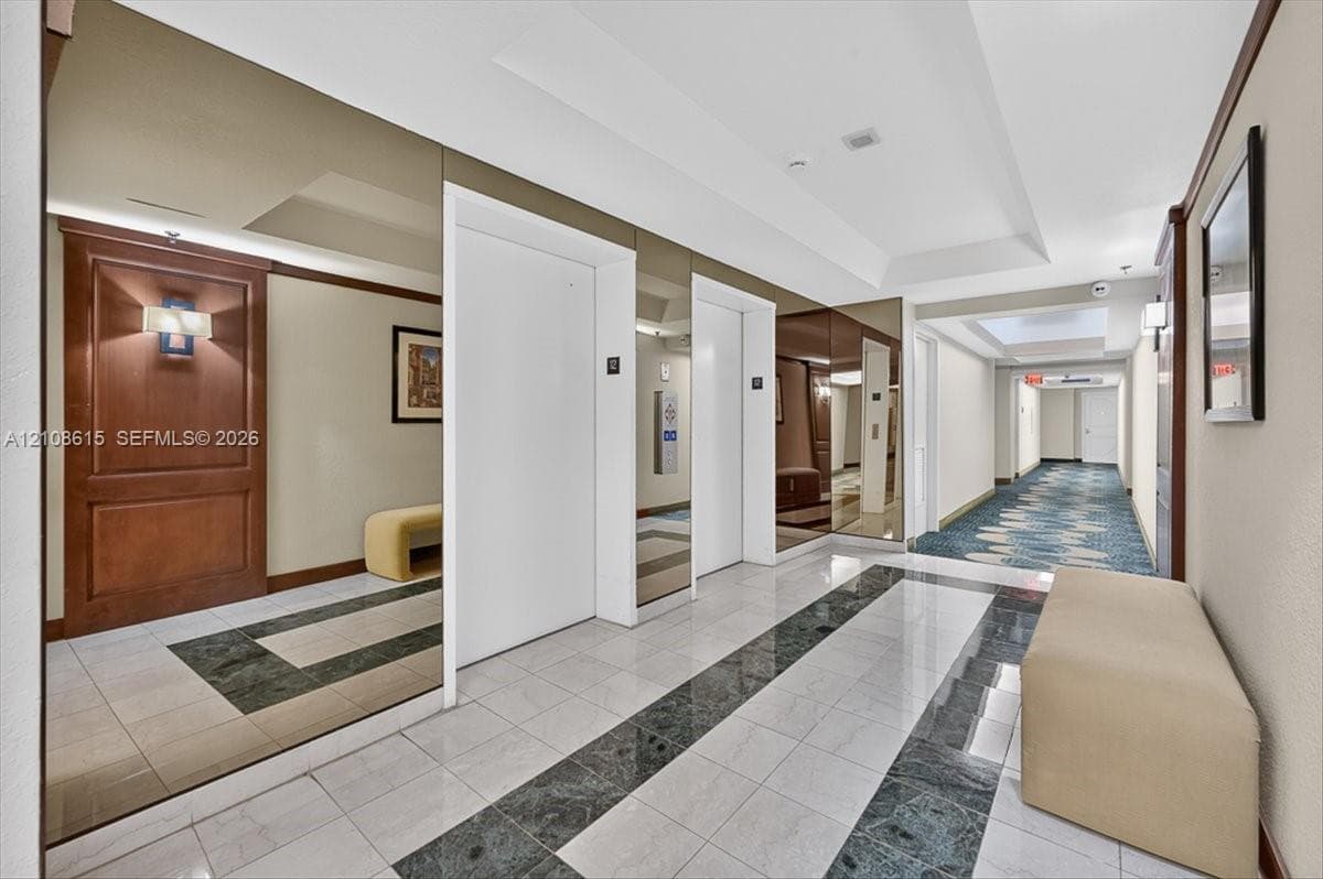 Elevator lobby featuring floor-to-ceiling wall mirrors, polished stone tile flooring with decorative inlay, and wood-paneled accents