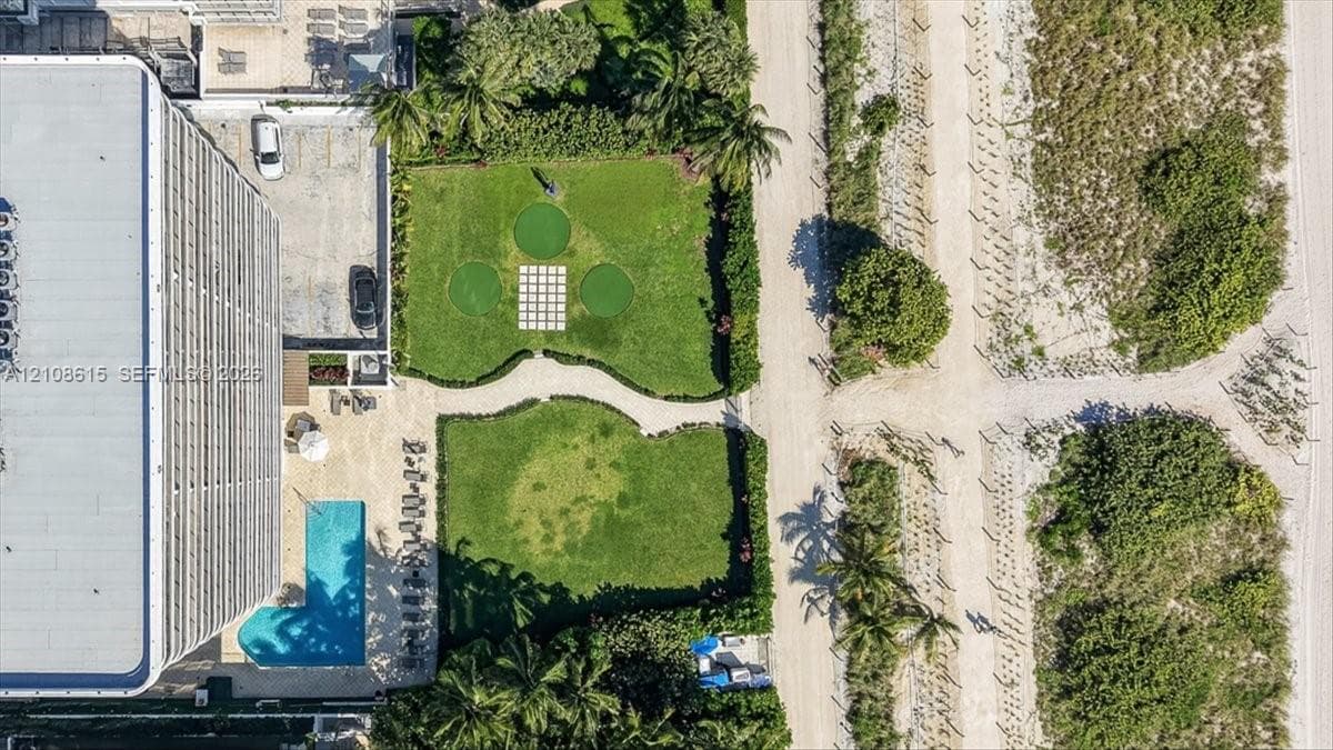 Aerial perspective of property grounds featuring an outdoor swimming pool, a putting green, paved walkways, and mature landscaping