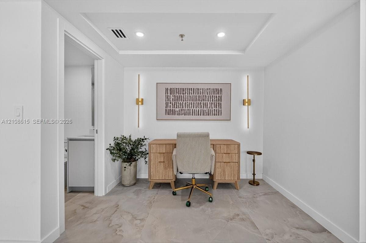 Room featuring large-format tile flooring, a recessed tray ceiling, and dual wall-mounted metallic light fixtures
