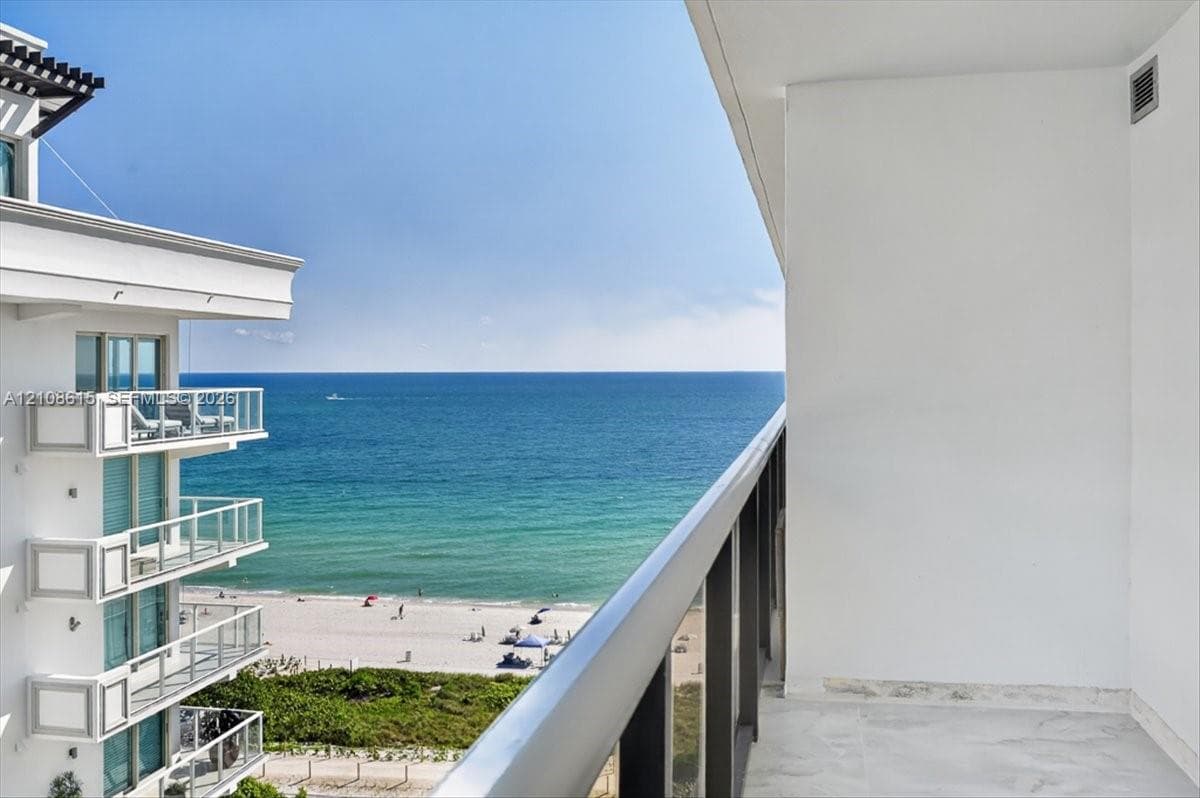 Private balcony with stone flooring and a glass-paneled railing overlooking the ocean and coastline