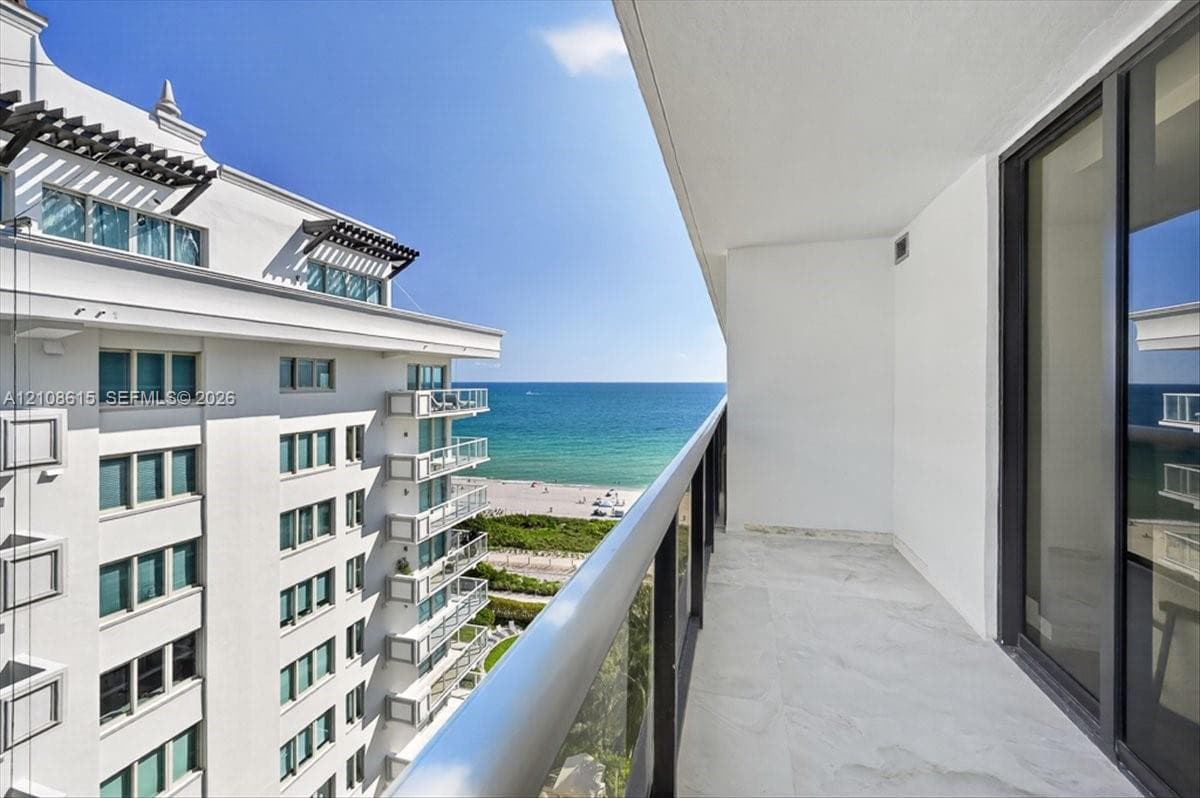 Private covered balcony featuring stone flooring and a glass panel railing, oriented toward the ocean