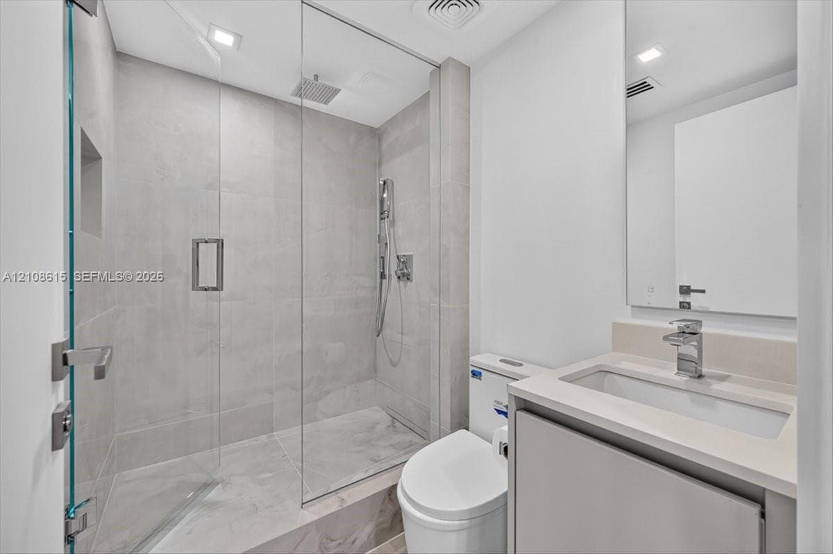 Bathroom featuring a glass-enclosed shower with a rainfall showerhead, large-format tile surround, integrated shower niche, wall-mounted vanity with a rectangular sink, and polished chrome fixtures