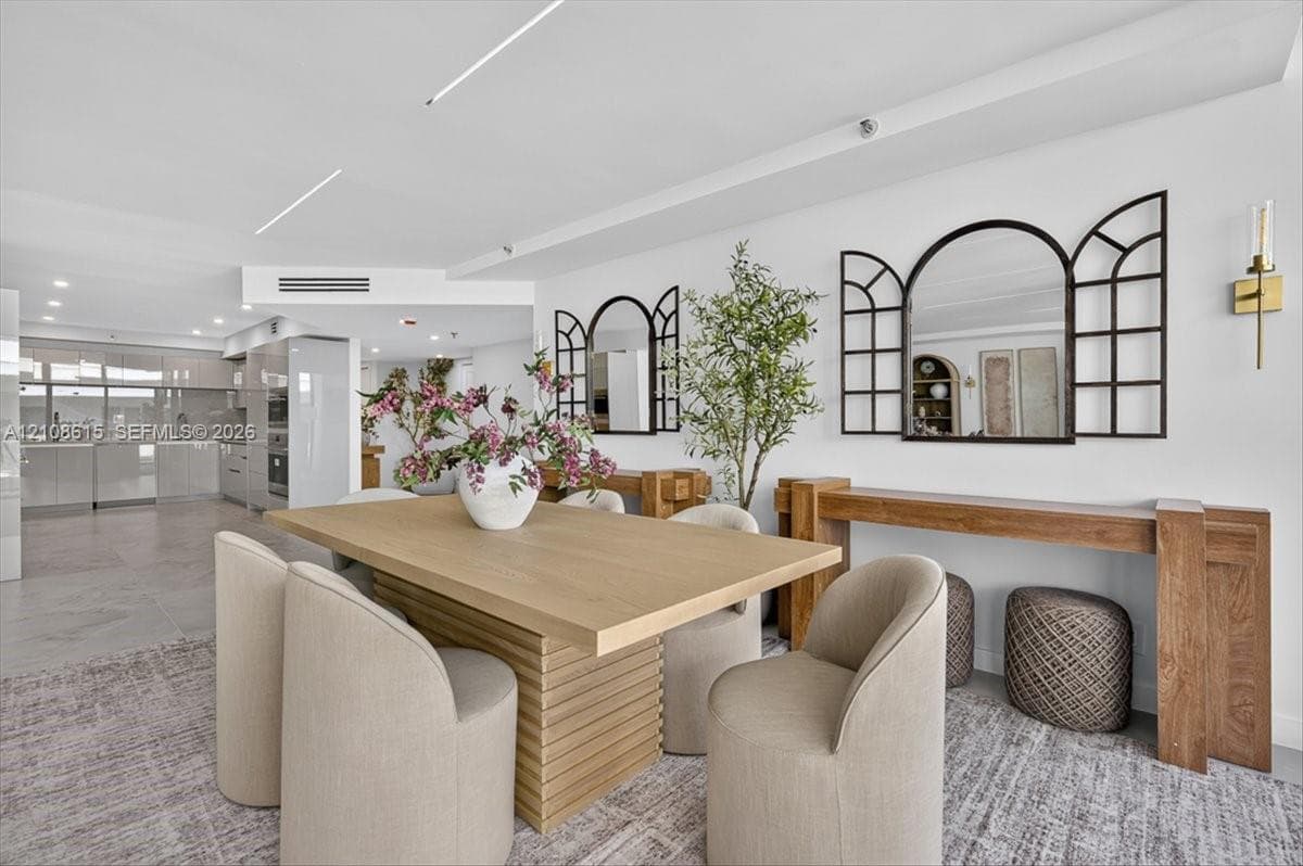 Open-concept living space featuring high-gloss cabinetry, linear recessed lighting, stone-finish flooring, and wall-mounted brass light fixtures