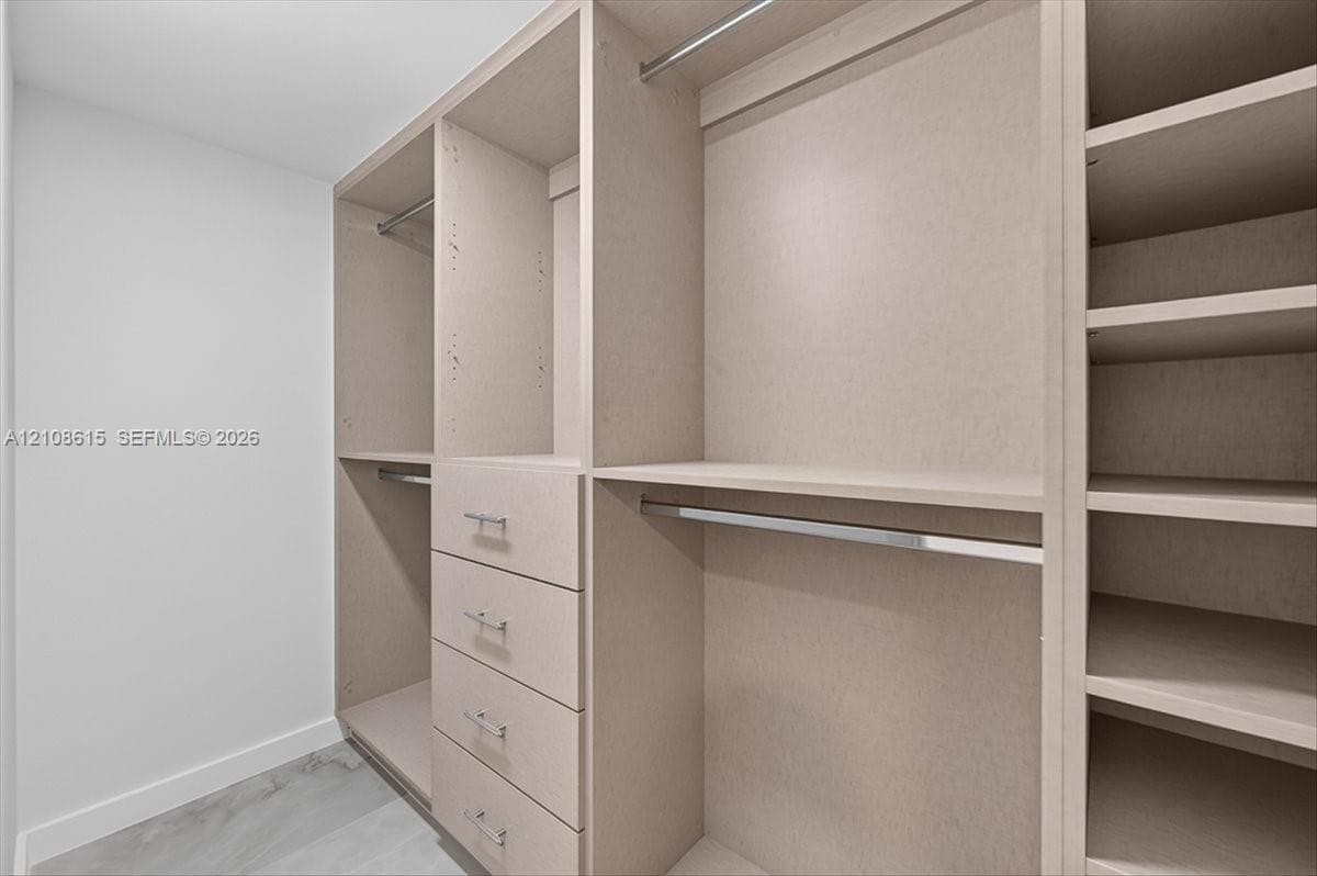 Custom reach-in closet featuring light-toned cabinetry, four integrated storage drawers, chrome hardware, multiple shelving tiers, and brushed metal hanging rods
