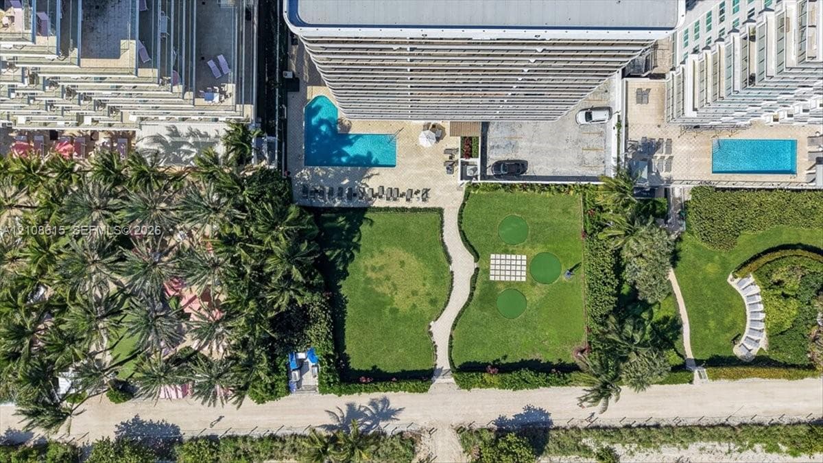 Aerial perspective featuring a swimming pool, manicured lawn areas, paved walkways, and integrated recreational turf spaces