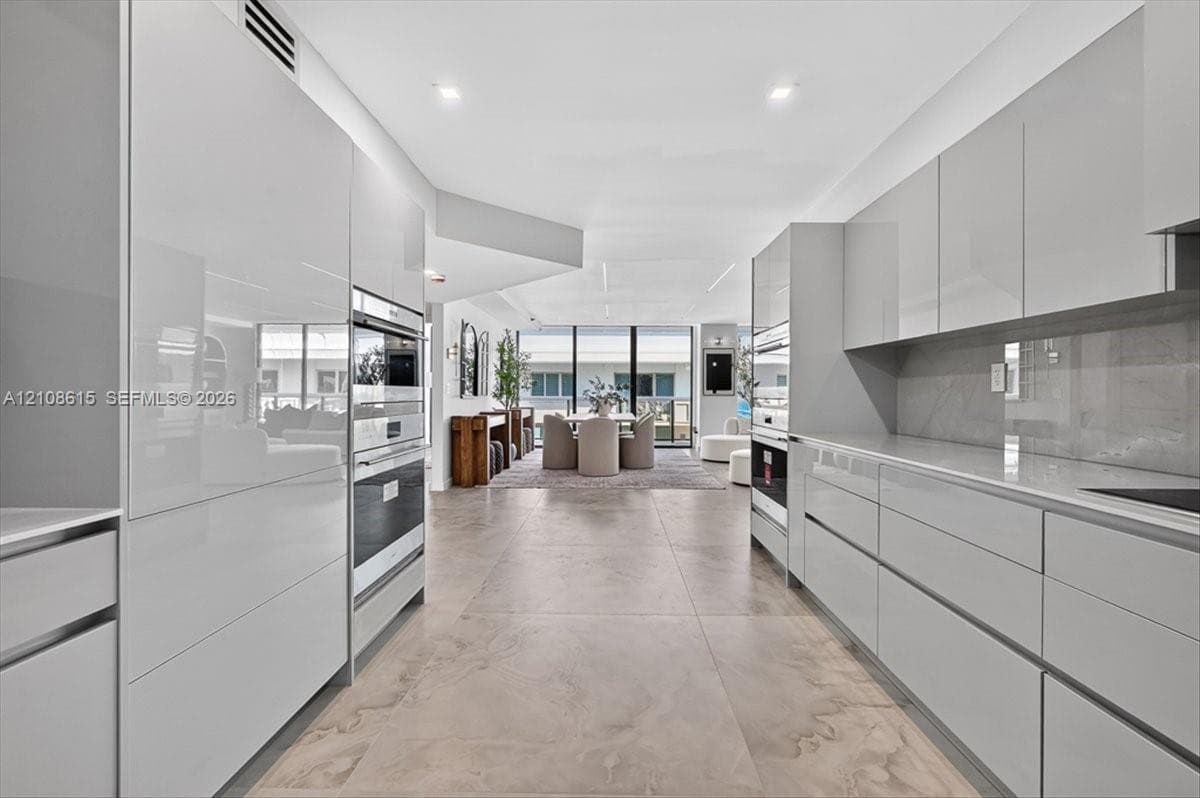 Contemporary kitchen featuring high-gloss cabinetry, large-format tile flooring, stone-surfaced countertops, and built-in stainless steel double ovens