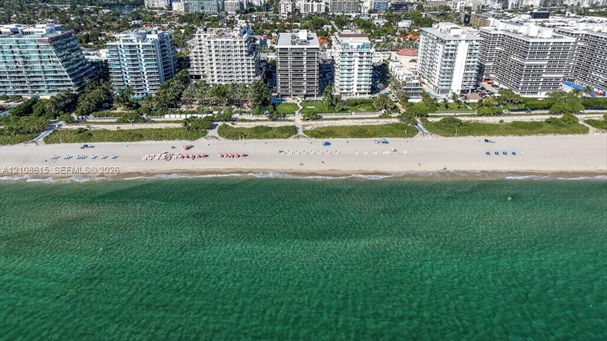 Aerial perspective of beachfront property featuring direct sand access, paved walkways, landscaped grounds, and coastal waters