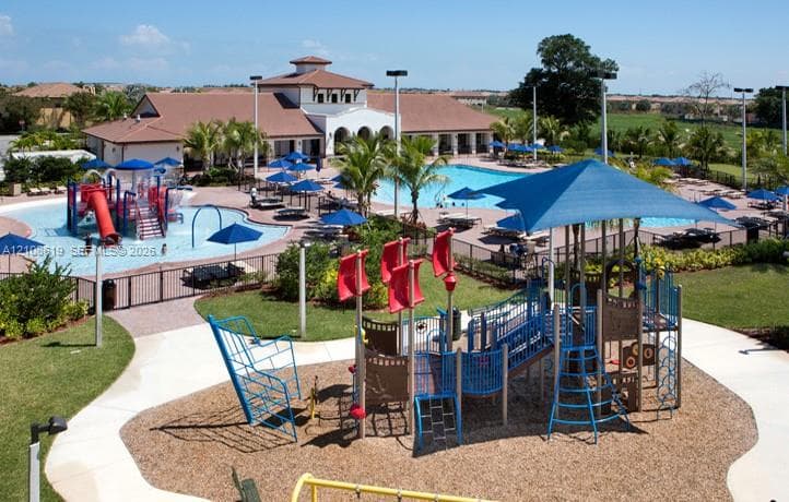 Community recreation area featuring an expansive swimming pool, a splash pad with water features, a shaded jungle gym, and a clubhouse facility