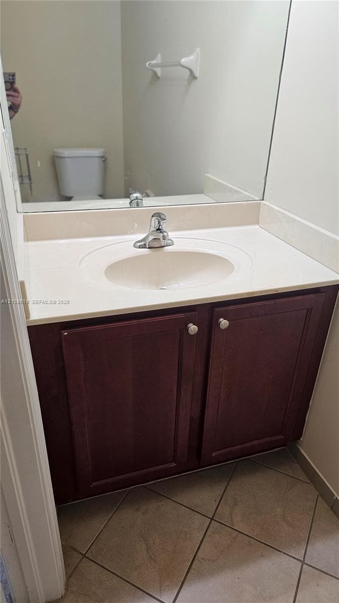 Bathroom vanity featuring a dark wood-finish cabinet, integrated basin, countertop with matching backsplash, and tile flooring