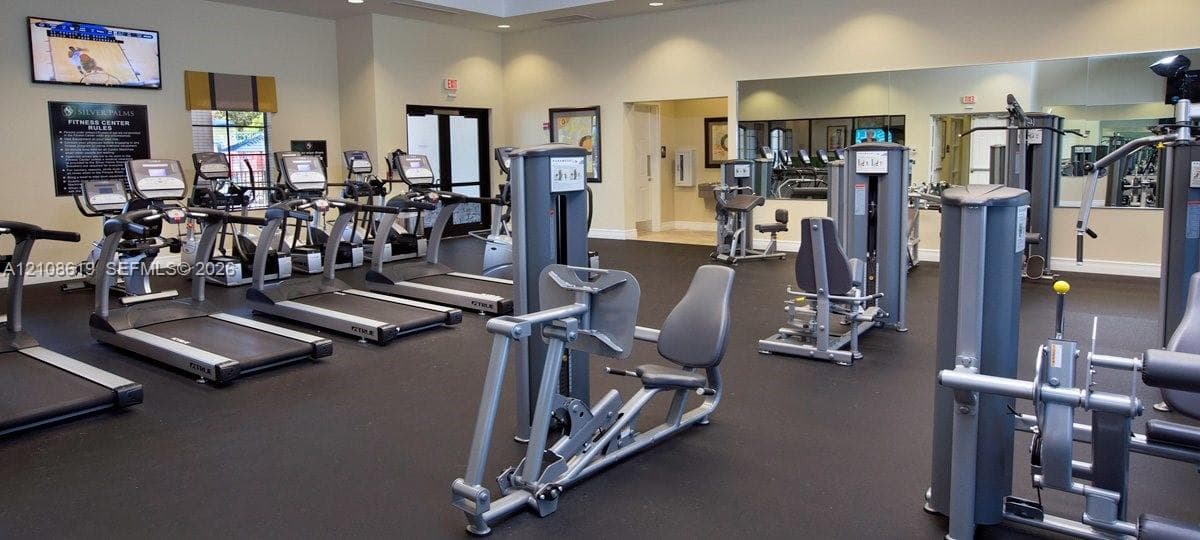 Fitness center featuring rubber flooring, wall-to-wall mirrors, and a selection of cardio and strength training equipment