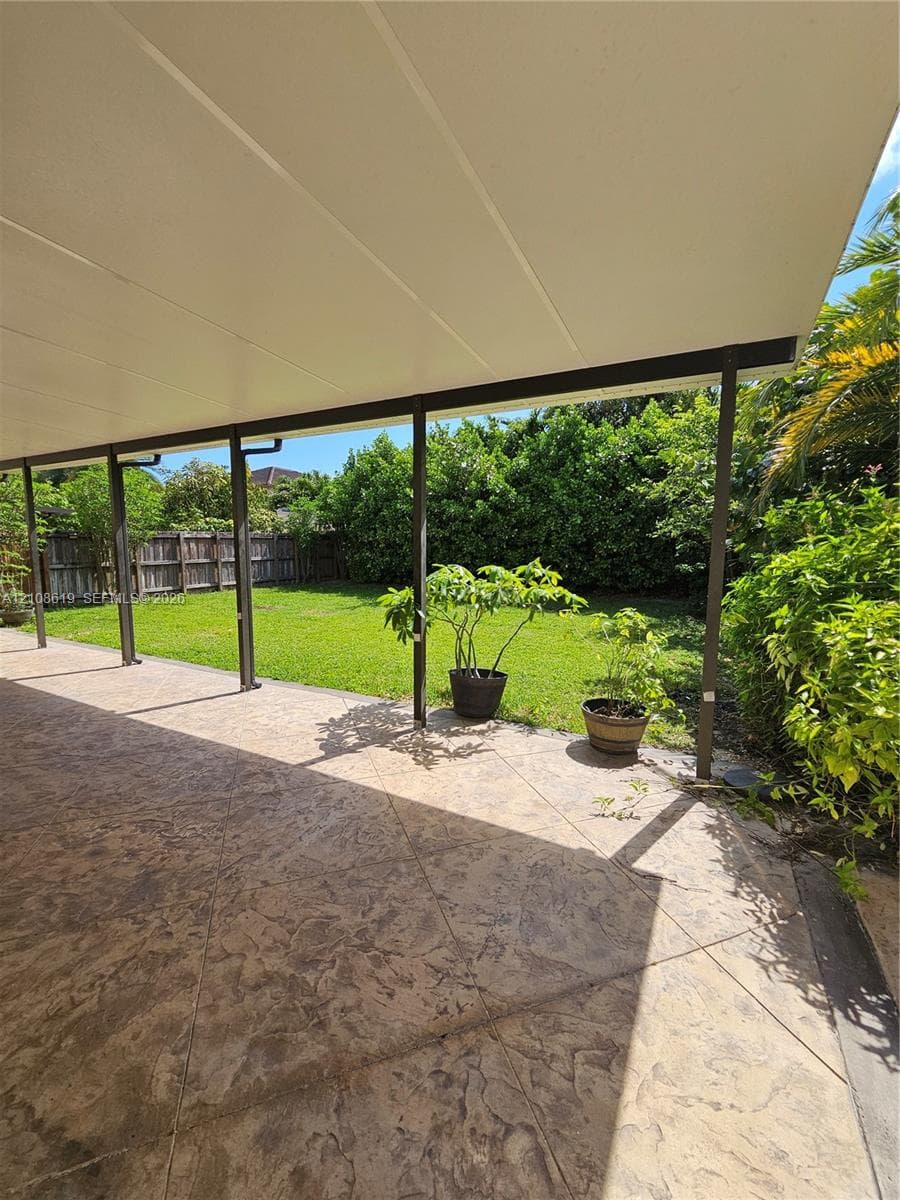 Covered patio with stamped concrete flooring, grass lawn, and perimeter wood fencing
