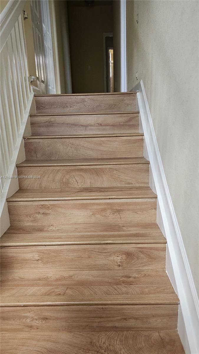 Staircase featuring wood-finish flooring treads and white painted handrails with matching vertical balusters