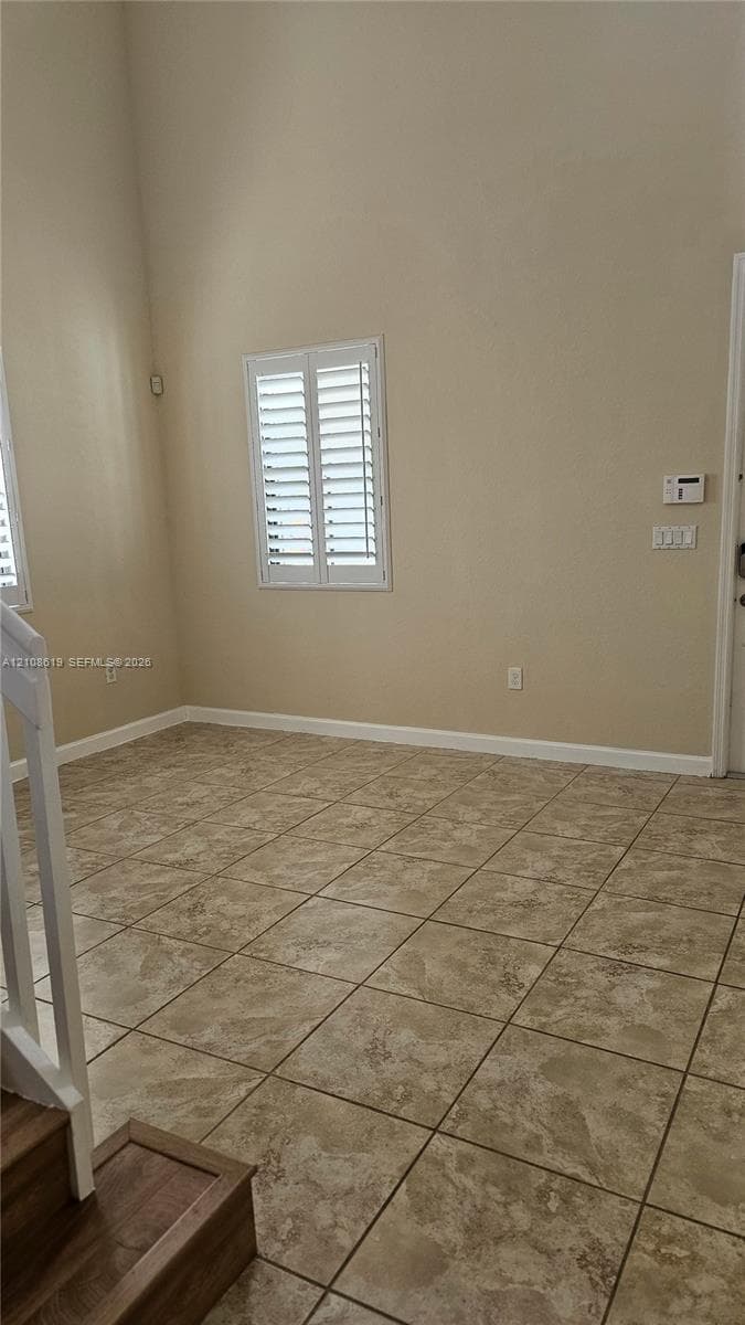 High-ceiling interior featuring tiled flooring, plantation shutters, and a wood-finish staircase railing