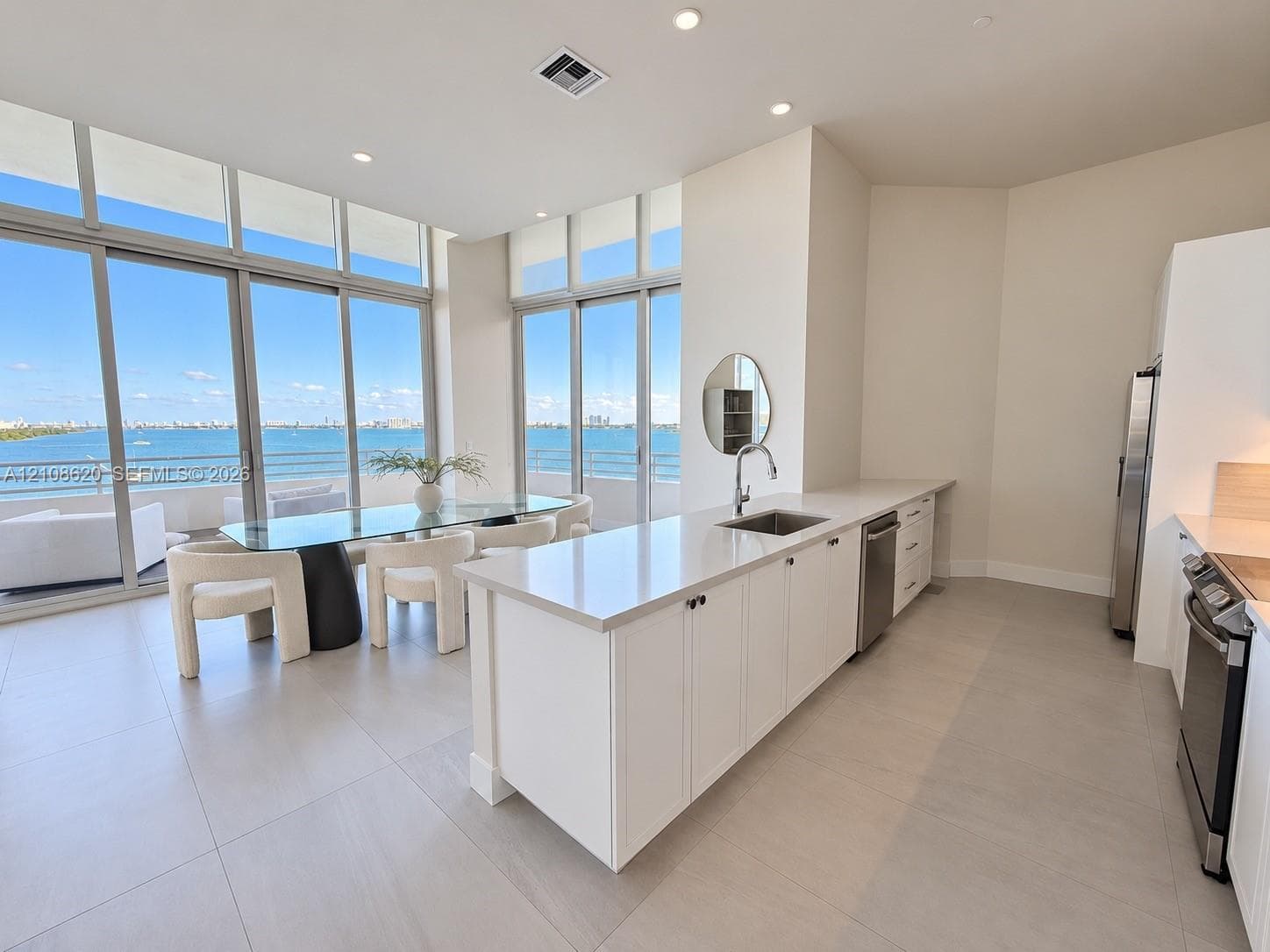 Kitchen featuring white cabinetry, solid-surface countertops, stainless steel appliances, large-format tile flooring, and floor-to-ceiling glass sliding doors