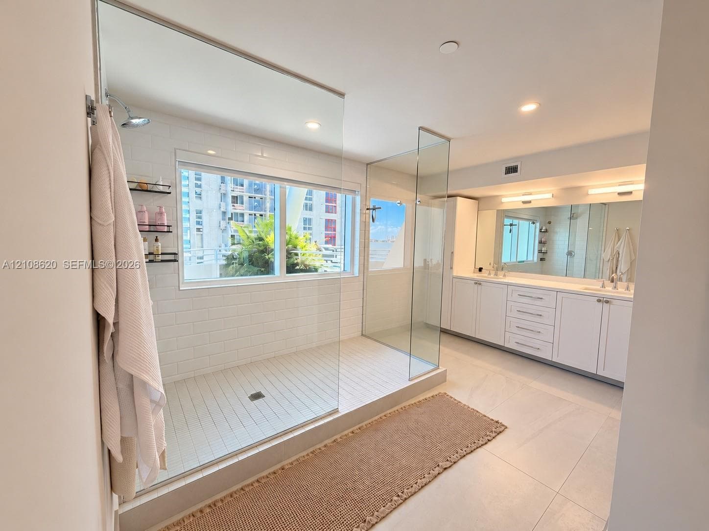 Walk-in shower with floor-to-ceiling glass enclosure, subway tile surround, dual vanity with extensive storage cabinetry, expansive wall-to-wall mirror, and oversized tile flooring