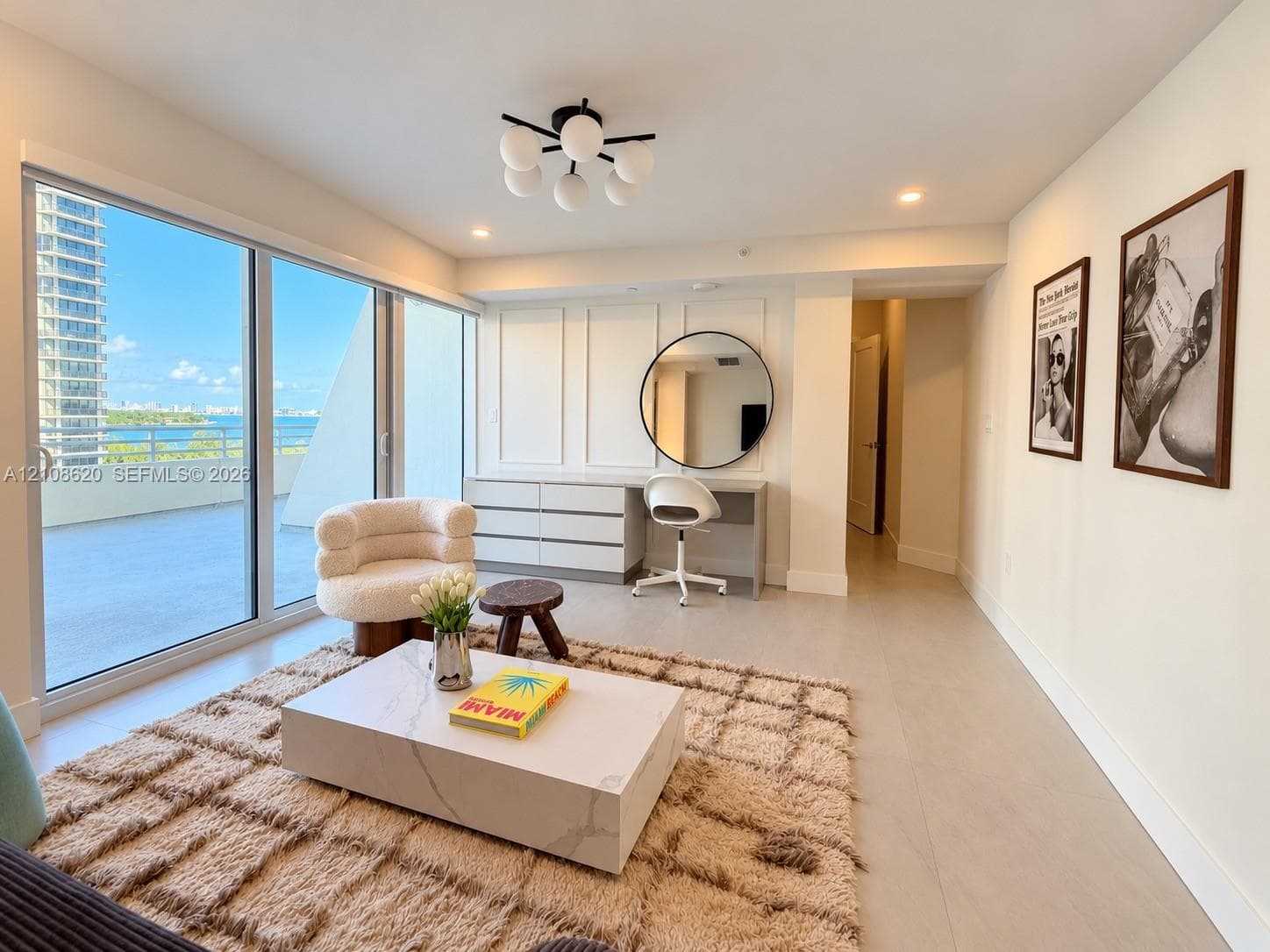 Floor-to-ceiling glass sliding doors, built-in desk with paneled millwork, circular wall mirror, contemporary multi-bulb ceiling fixture, and neutral-tone flooring