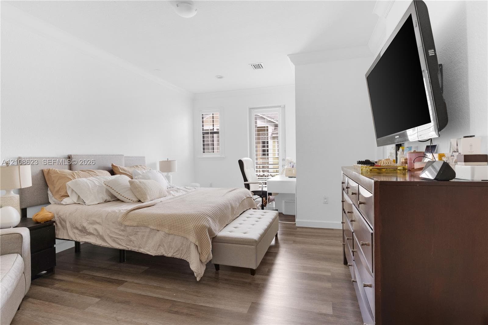 Bedroom featuring wood-finish flooring, crown molding, plantation shutters, and a glass-paneled door